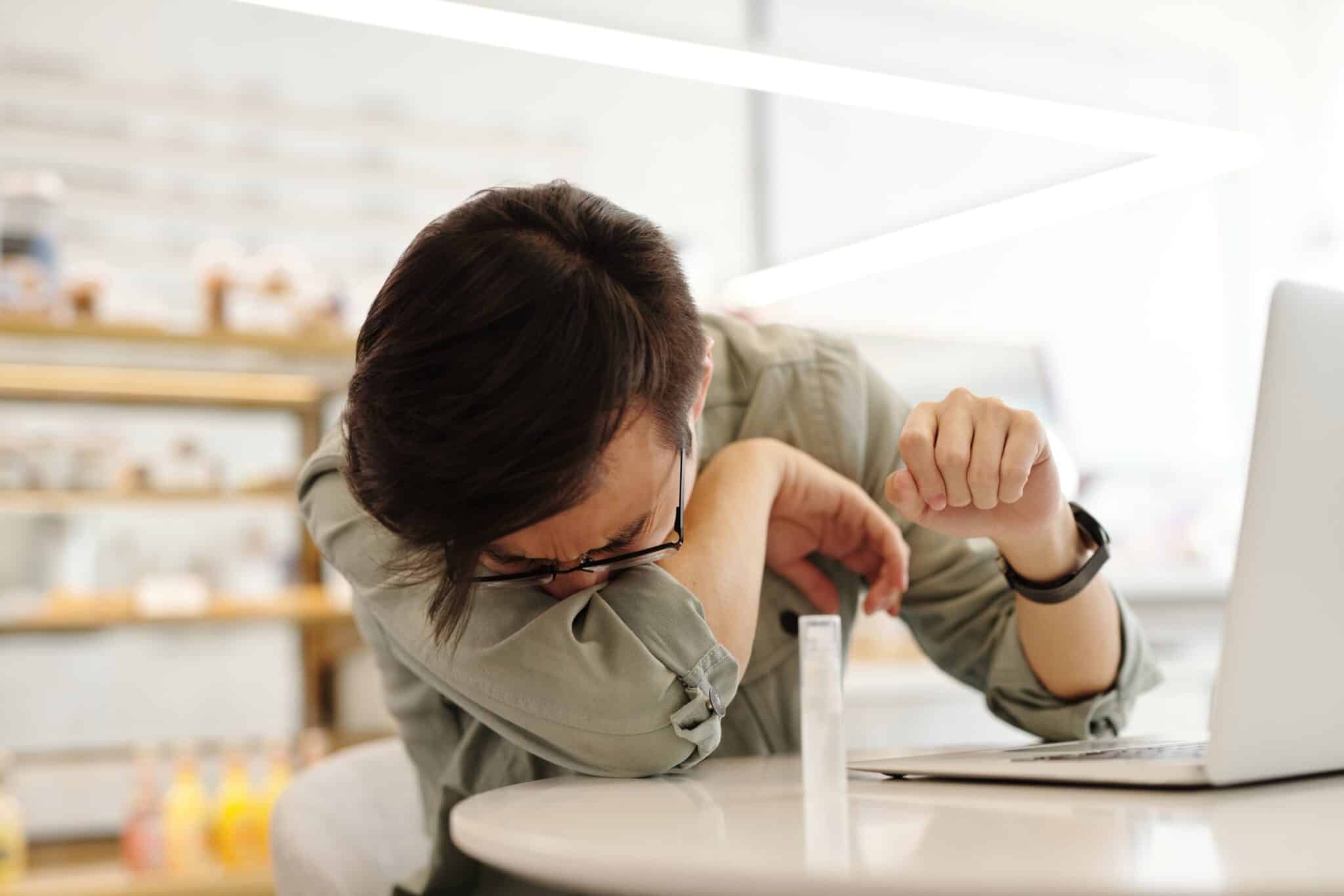 Man sneezing into his arm while out at a cafe.