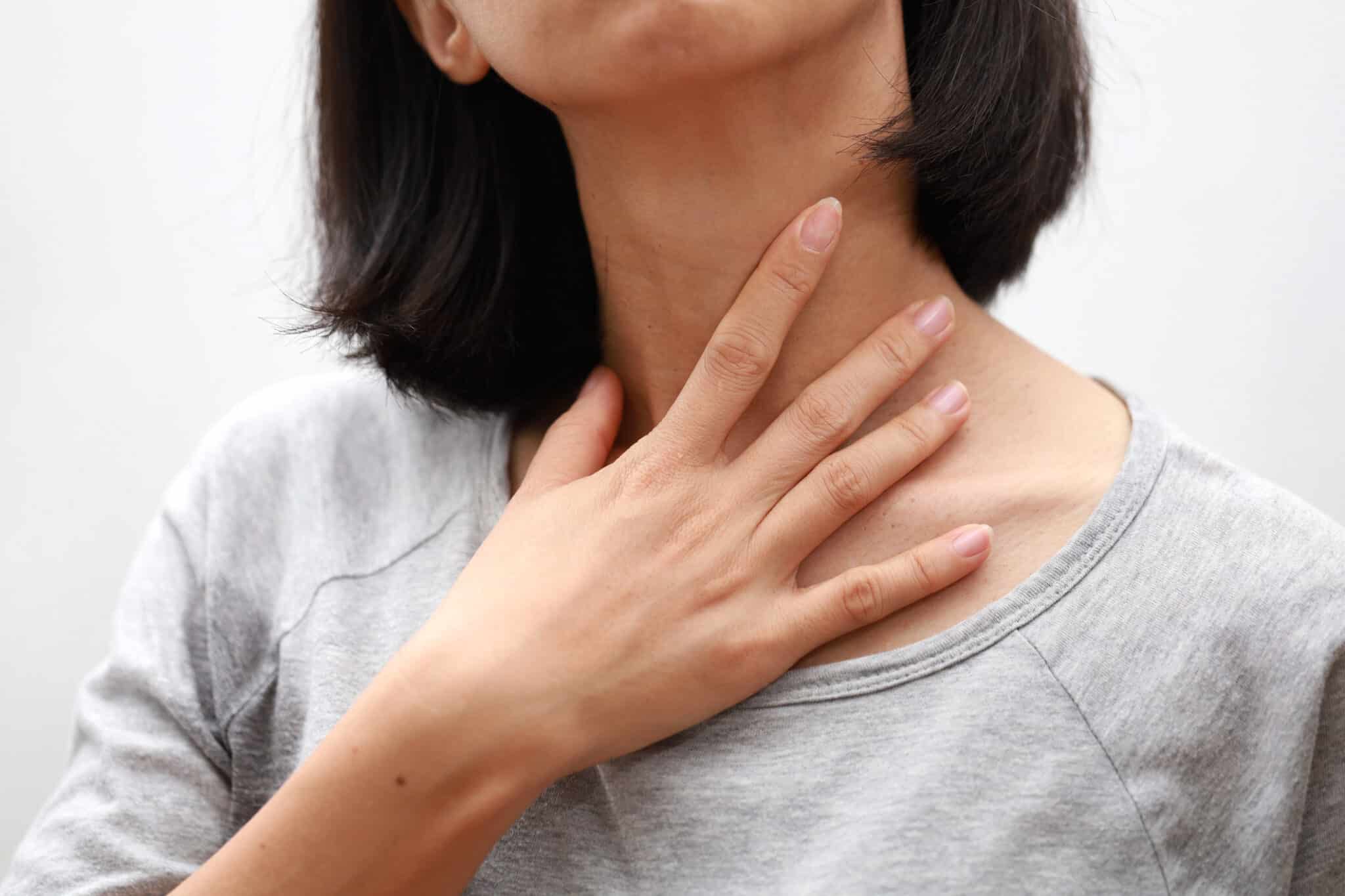 Closeup of woman touching her sore throat.