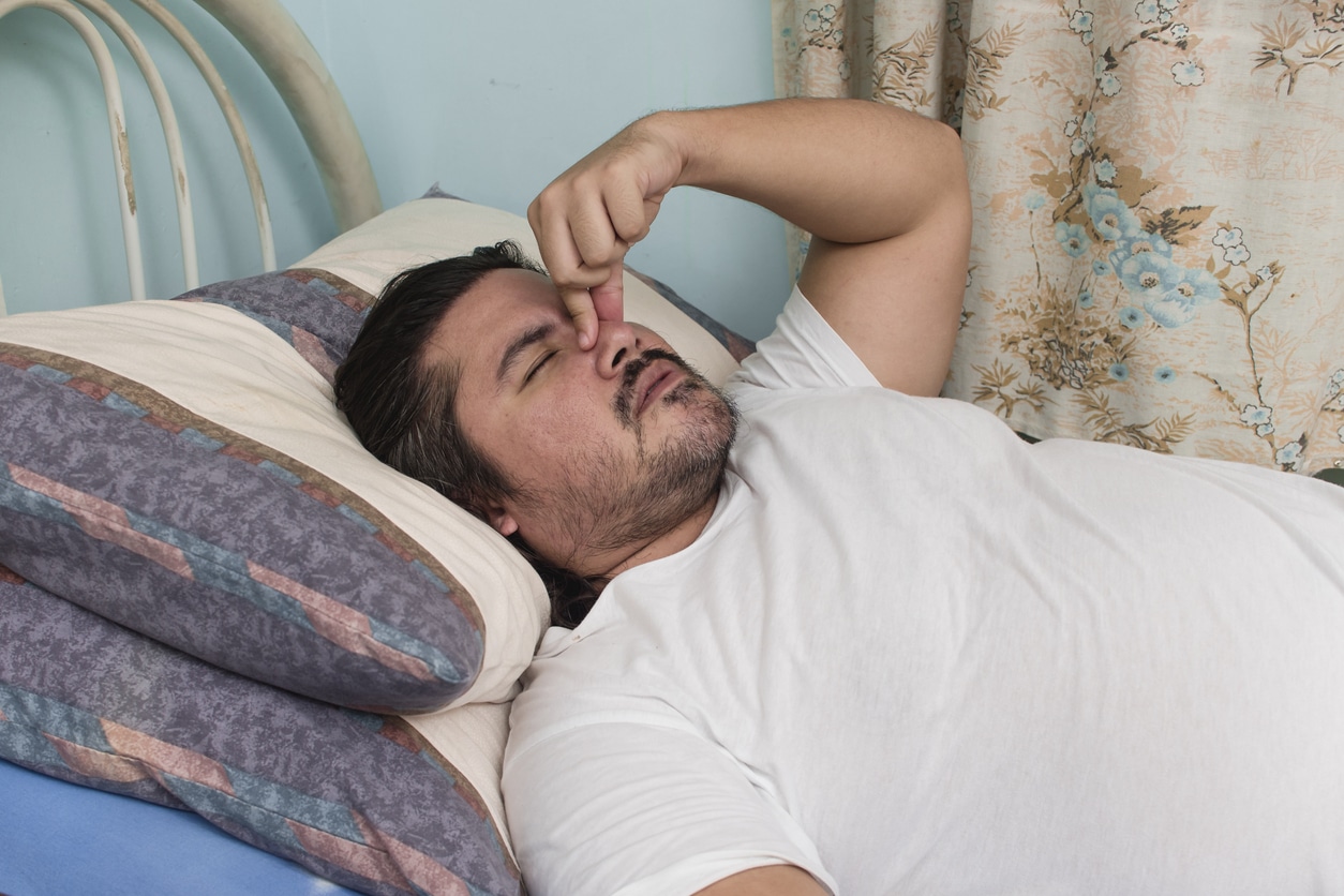 Man in bed, waking up with a stuff nose.