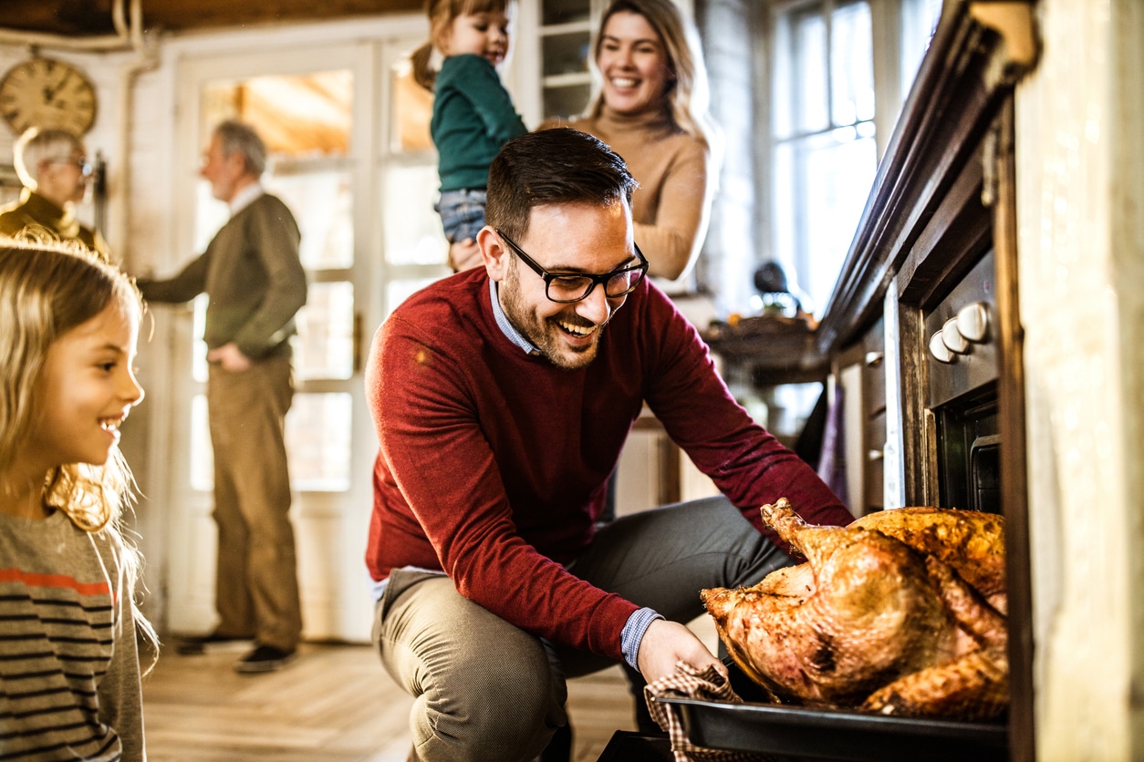 Man taking a Thanksgiving turkey out of the oven surrounded by his family