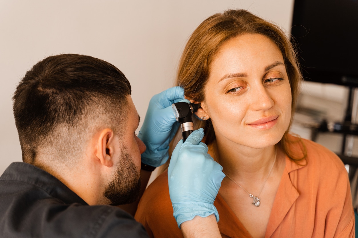 Otolaryngologist looks through otoscope the ears of woman