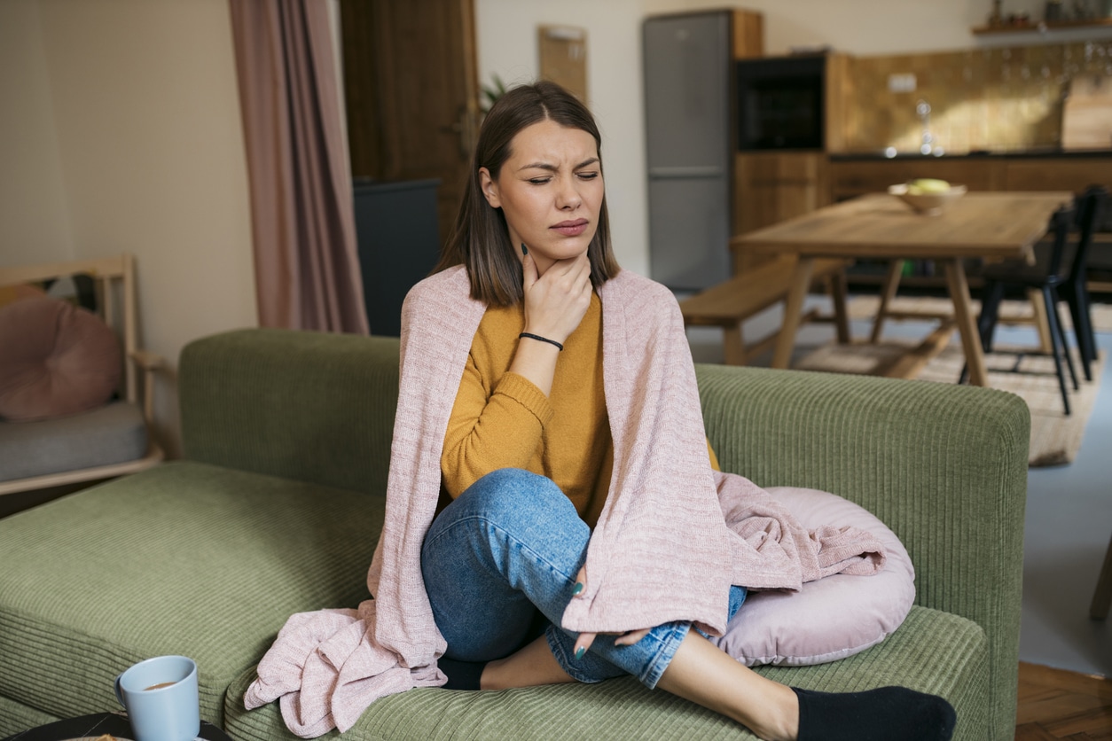 Woman suffering from sore throat sitting on sofa
