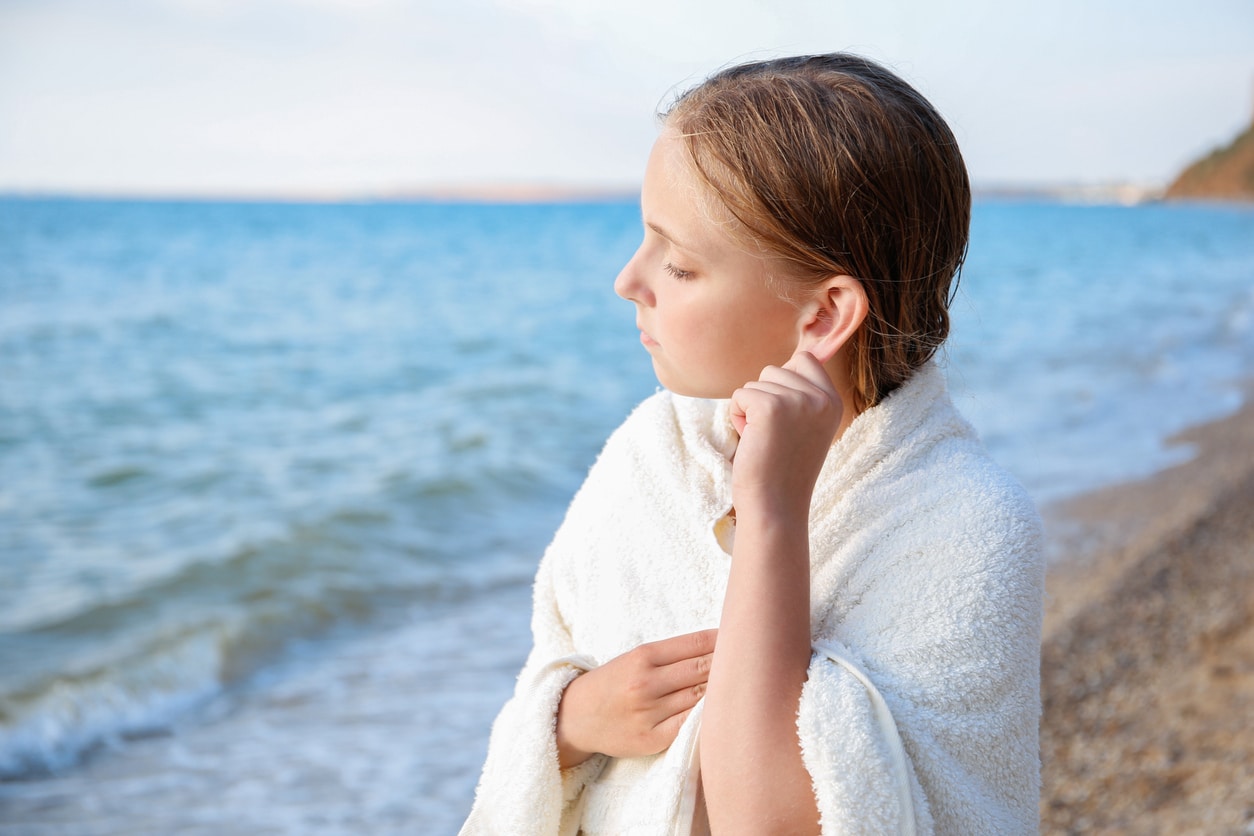 Young girl at the beach tugging on her ear, trying to get water out