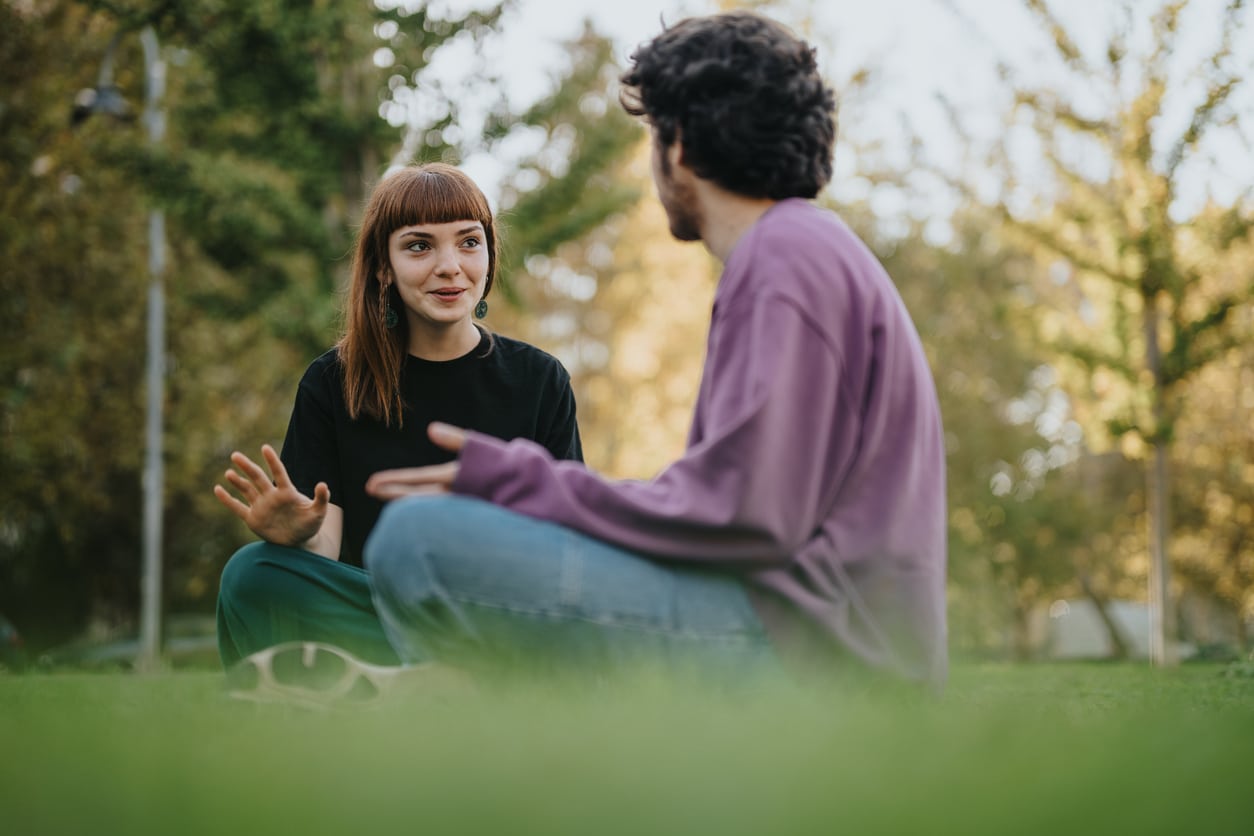 Young friends sitting on grass, enjoying conversation outdoors in bright sunlight