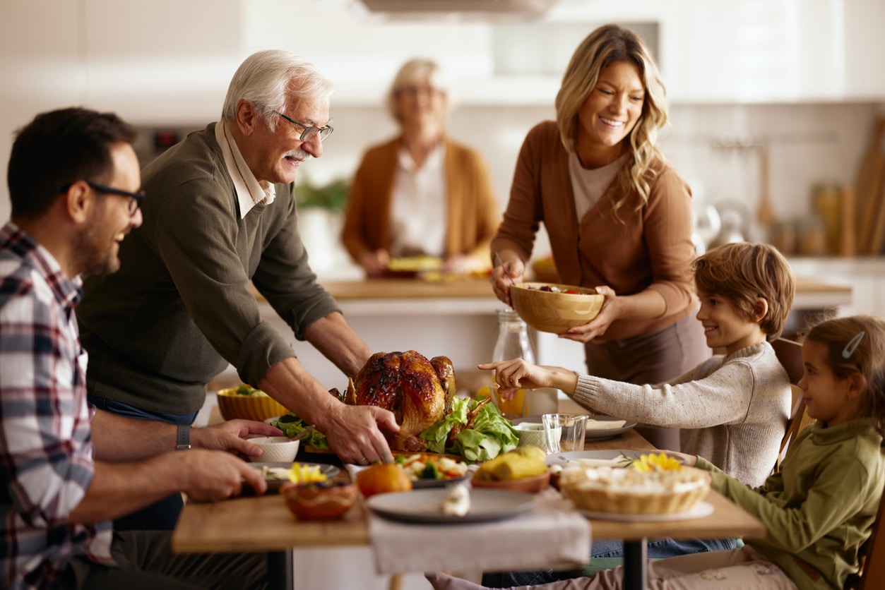 Happy senior man and his daughter serving Thanksgiving lunch to their family